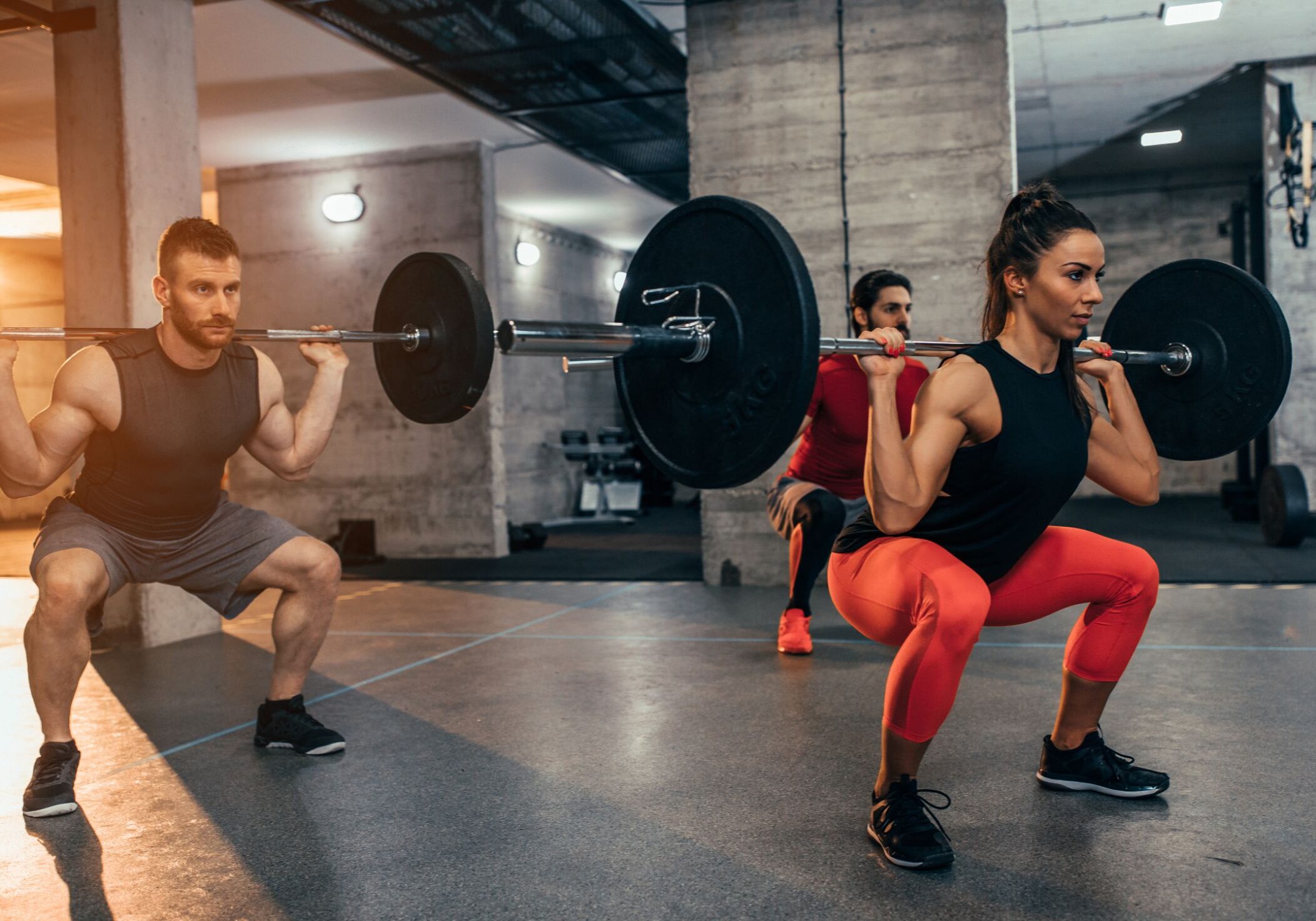 People doing barbell squats at the gym.